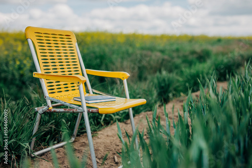 Yellow folding chair with a blue book in a spring wheat field