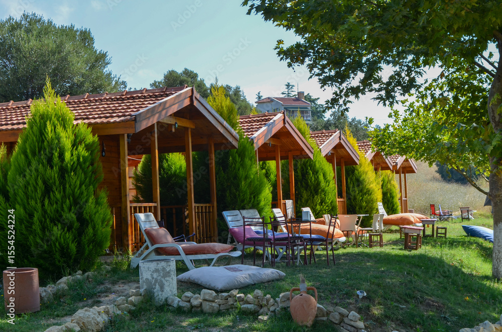 Obraz premium A small wooden house with a porch and a patio. The house has a wooden roof and a wooden door. The patio has a table and chairs, and a few lounge chairs. The lawn is green and well-maintained
