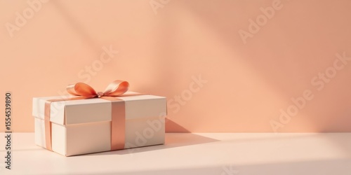 A delicately wrapped gift box with a soft peach ribbon, sitting on a light surface against a pale orange backdrop, bathed in sunlight