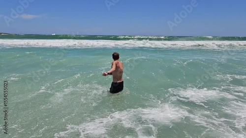 Man is swimming in the ocean. The water is blue and the sky is clear. The man is wearing a black shirt and shorts