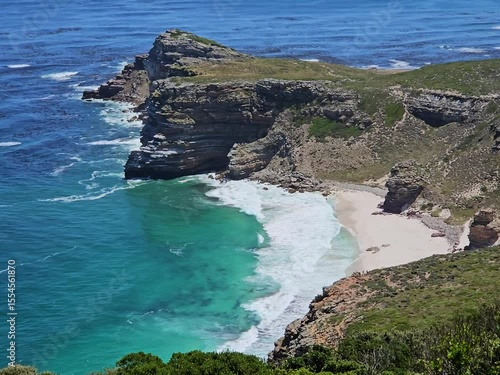 Rocky cliff overlooks a beach and ocean. The water is blue and the beach is sandy in Cape of good hope in South Africa