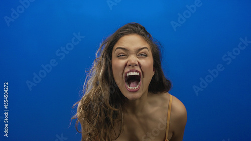 Εκτύπωση καμβά Hispanic young woman with curly hair in orange bikini screams with open mouth and visible teeth in studio; anger