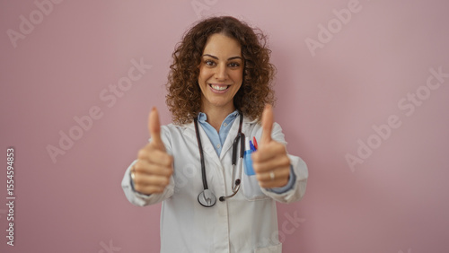 Schilderij op canvas Woman doctor smiling with curly hair giving thumbs up wearing white coat isolated on pink background representing healthcare and positivity