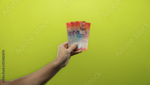 Canvas Print Hand of a man holding swiss franc banknotes against an isolated yellow background, showcasing colorful currency from switzerland in a clear and vibrant close-up view