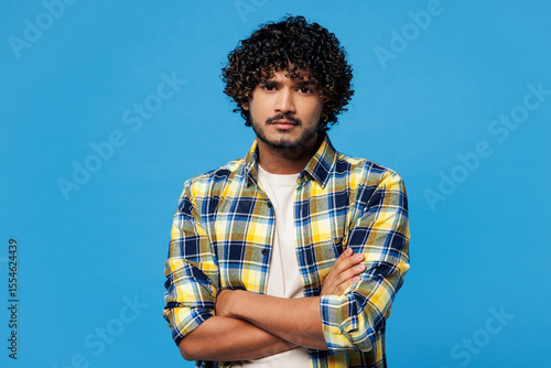 Photos Young sad mad frowning Indian man he wearing yellow checkered shirt casual clothes hold hands crossed folded looking camera isolated on plain blue cyan background studio portrait