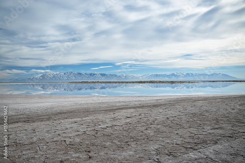 Vibrant autumn-sky hues paint the shoreline of Utah’s Great Salt Lake. Calm blue waters mirror cotton‑cloud skies, while distant mountains stand quietly, embracing seasonal wonder.