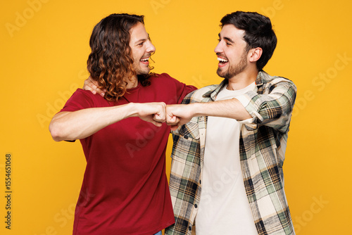 Tableau sur toile Young smiling happy two friends buddies men they wearing casual clothes together look camera do fist bump gesture isolated on plain yellow orange color background studio portrait