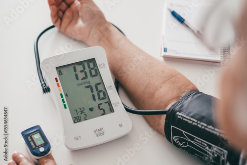 Elderly woman using medical device to measure blood pressure - senior woman suffering from hypertension sitting at home table taking care of her health