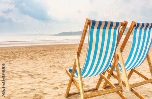 Wooden deck chairs on a sandy beach with a headland in the distance.