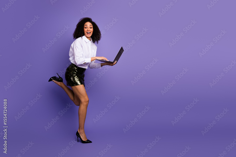 Fototapeta premium Joyful young businesswoman in stylish formalwear jumping with a laptop against a purple background, promoting success