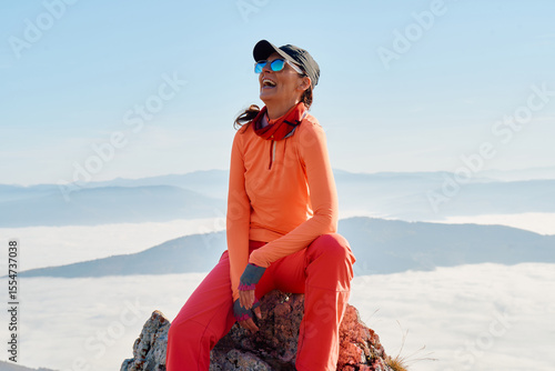 A female hiker enjoys the serene beauty of the mountain landscape, sitting on a rock at the summit, surrounded by breathtaking scenery and a sense of tranquility.