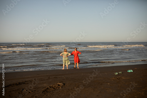 Senior mother and adult daughter enjoy quality time by the sea, barefoot on a sunny beach, sharing smiles and the joy of travel, connection, and warm memories.