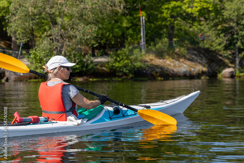 Foto Woman paddling close to a rocky shoreline covered in greenery