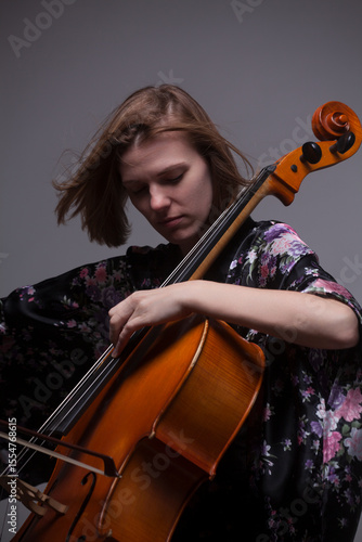 Woman playing cello, wearing floral robe, studio shot.