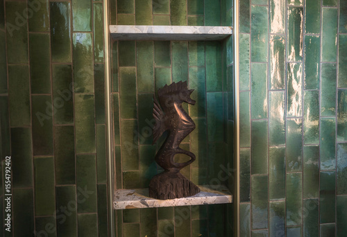 Turquoise tiled bathroom wall with a vintage wooden seahorse statue displayed on a shelf. A playful, retro accent with high end mid-century charm.