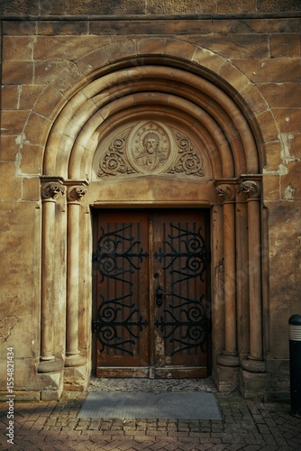 Old Romanesque church door with ornate ironwork and a carved stone arch featuring a religious icon relief above the entrance.