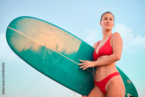 Canvas Print happy young woman with an athletic build smiles holding her longboard on the bea