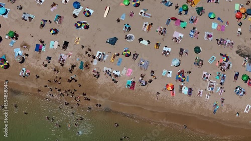 Aerial drone top down view of a crowded beach with colorful umbrellas and sunbathers during a summer afternoon near the coast