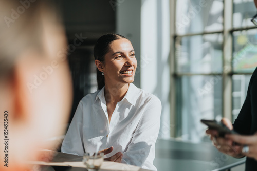 A cheerful businesswoman in a white shirt enjoys a conversation in a bright office kitchen, fostering a welcoming and collaborative atmosphere. Ideal for business, teamwork, and professional