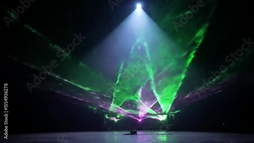 A vibrant laser light show illuminates a dark stage with dynamic green and purple beams