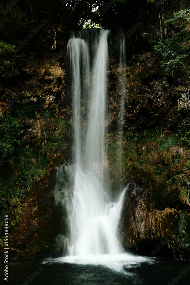 Obraz premium Veliki Buk waterfall in Lisine reserve, Serbia, with a strong vertical flow cascading over mossy cliffs into a clear pool below. Captured with a soft long exposure effect.