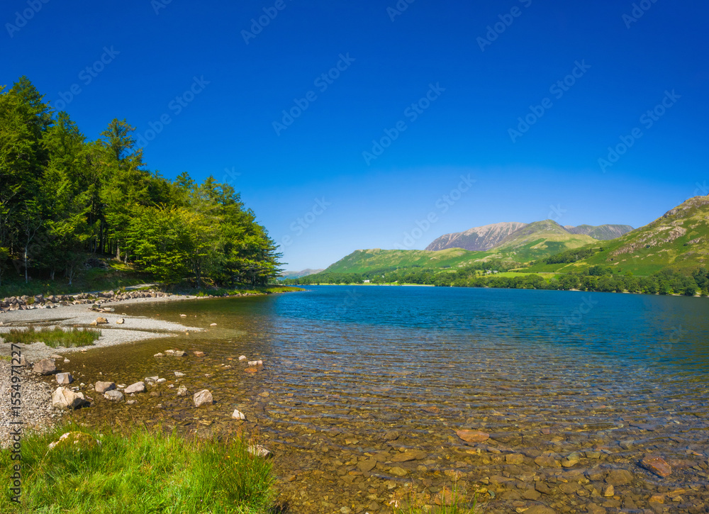 Naklejka premium Gravel lakeshore with clear water and mountains in summer (Buttermere, Lake District, England, United Kingdom)