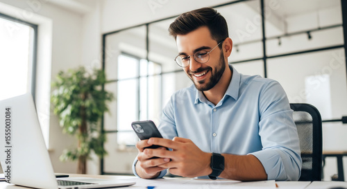 Smiling Man in Glasses Using Smartphone at Desk in Office