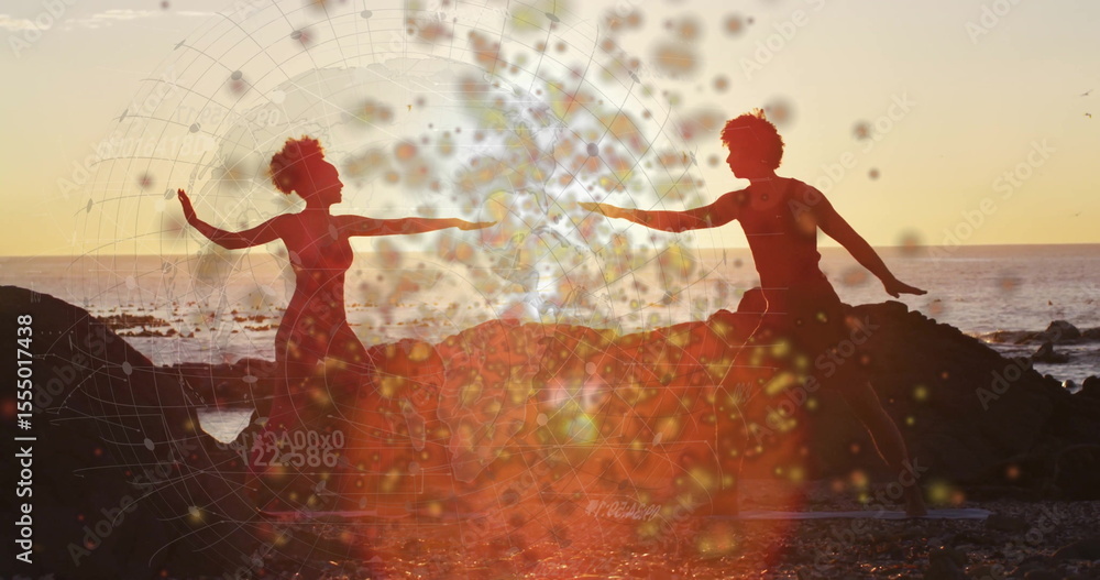 Obraz premium Dance duo performing mirrored yoga pose on rocky beach at sunset, with yoga mats, bokeh overlay