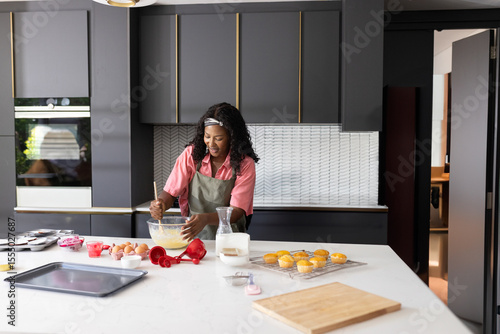 Fotografie African American woman in green apron mixing batter in glass bowl at kitchen isl