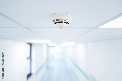 Shallow focus of smoke detection seen within a ceiling along a typical NHS hospital in Britain. The corridor branches to various wards.