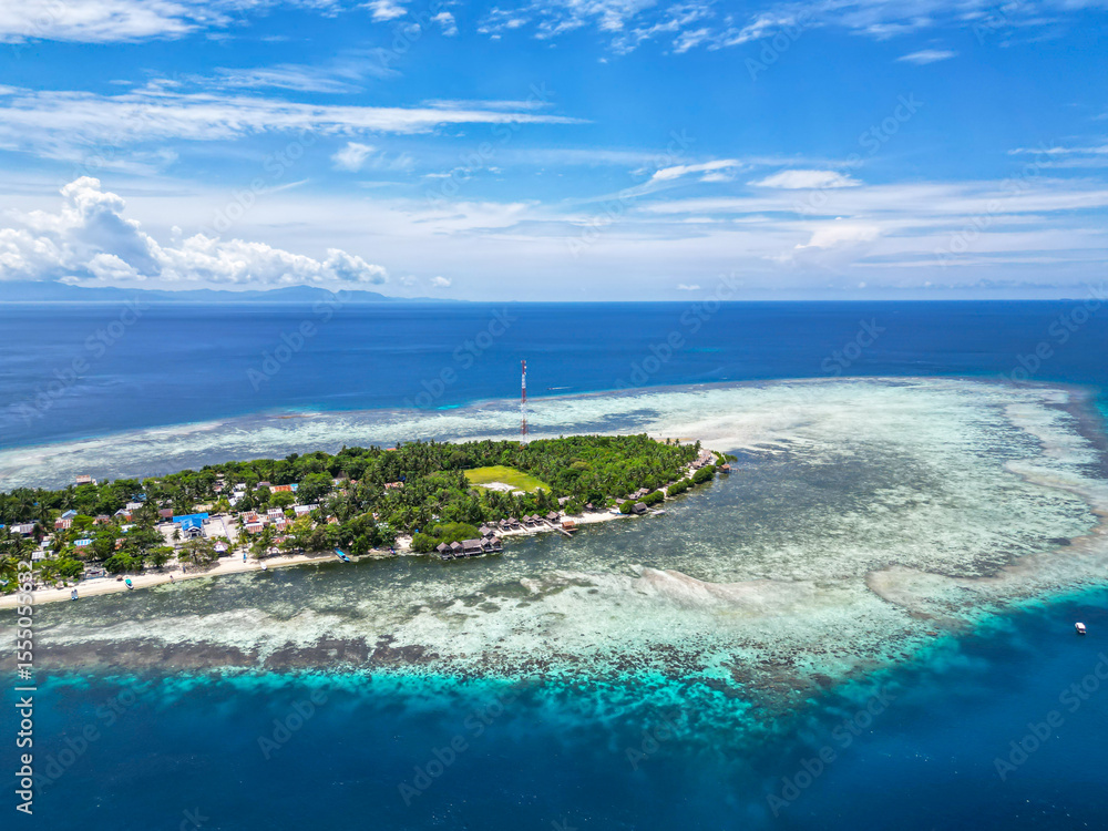Fototapeta premium Picturesque Tropical Island with Village and Jetty Surrounded by Clear Blue Waters and Coral Reefs in Indonesia