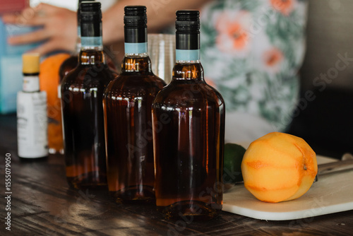 Bartender arranging amber spirits bottles on rustic wooden bar top next to peeled orange on marble cutting board