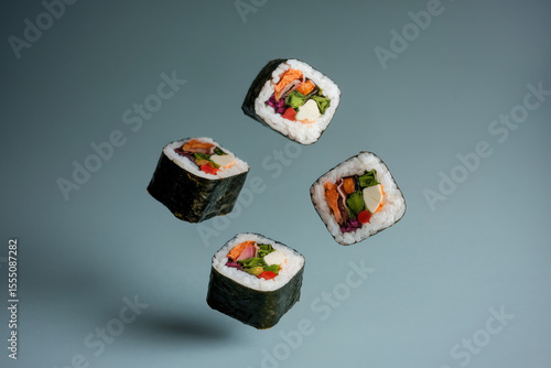 Colorful assorted sushi rolls with rich fillings floating on blue-gray background in modern minimal food photography concept