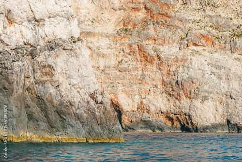 Glorious hues dance on the surface of the water, as towering limestone cliffs meet the calm sea at sunset. The serenity of this hidden gem invites contemplation and peace