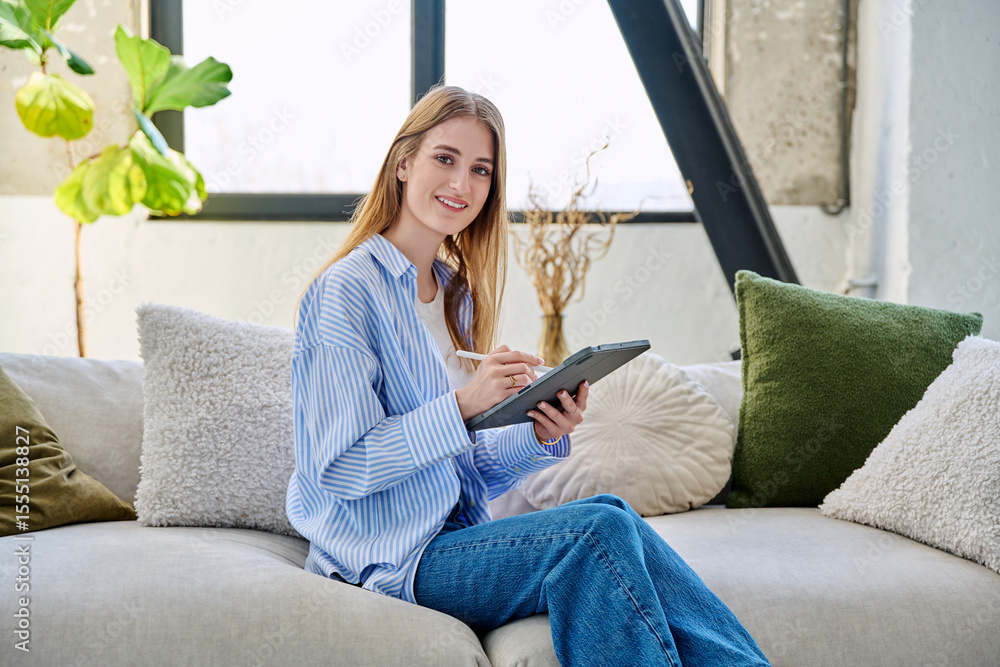 Obraz premium Young woman using digital tablet sitting on sofa at home