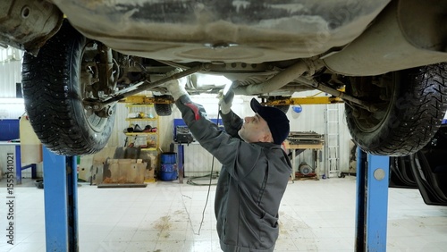 фотографія Experienced mechanic checking vehicle undercarriage with flashlight, working car
