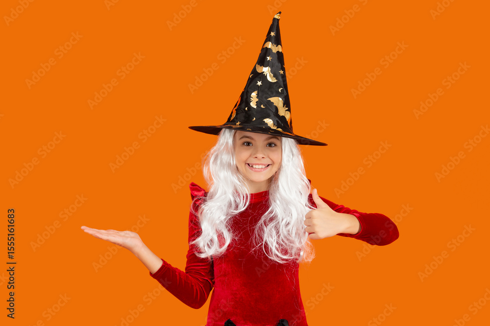 All Hallows advertisement. October 31. Girl in witch costume. Presenting product. Happy Halloween. Girl witch in Halloween costume isolated on orange. All Hallows holiday sale. Thumb up All Hallows advertisement. October 31. Girl in witch costume. Presenting product. Happy Halloween. Girl witch in Halloween costume isolated on orange. All Hallows holiday sale. Thumb up