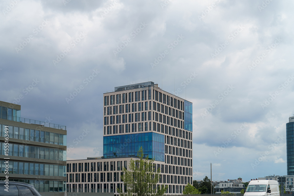 Modern office building with large windows against a cloudy sky in an urban setting Modern office building with large windows against a cloudy sky in an urban setting