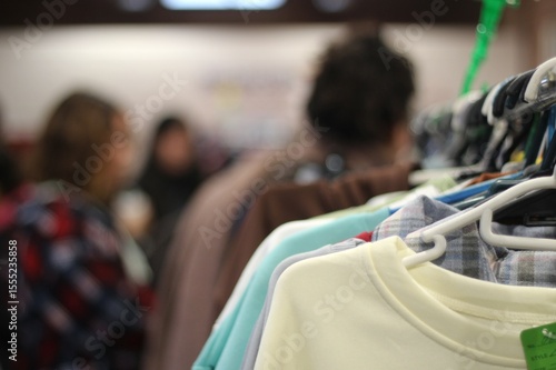 cabideiro com roupas de segunda mao, em feira de consumo consciente,  moda circular, com pessoas em fundo desfocado e dirigido. 