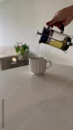 Hand pouring herbal tea into cup in peaceful home 