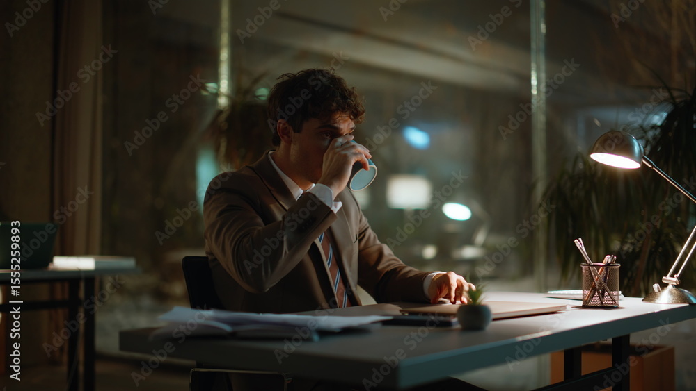 Evening manager drinking coffee at office under lamp light. Man making break Evening manager drinking coffee at office under lamp light. Man making break