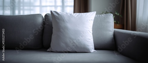 A poised white pillow accentuates a sleek grey couch by a window, casting soft shadows that emphasize a tranquil ambiance.