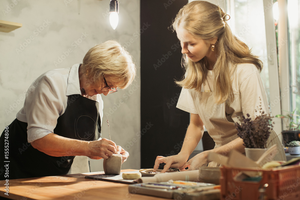 Fototapeta premium Senior woman learning pottery with young artisan in workshop