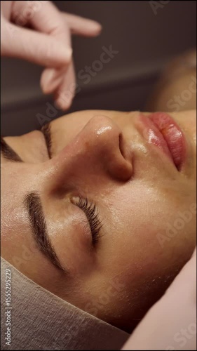 Beautician doing female anti-wrinkle rejuvenating facial massage in beauty salon, close-up, vertical