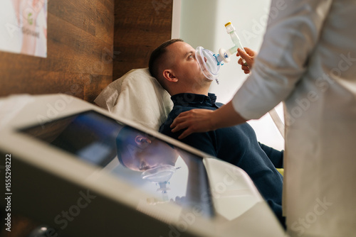 Obraz na plátně Side view of unrecognizable female doctor assisting to male patient undergoing respiratory training with oxygen mask, providing essential care and monitoring progress in modern medical clinic