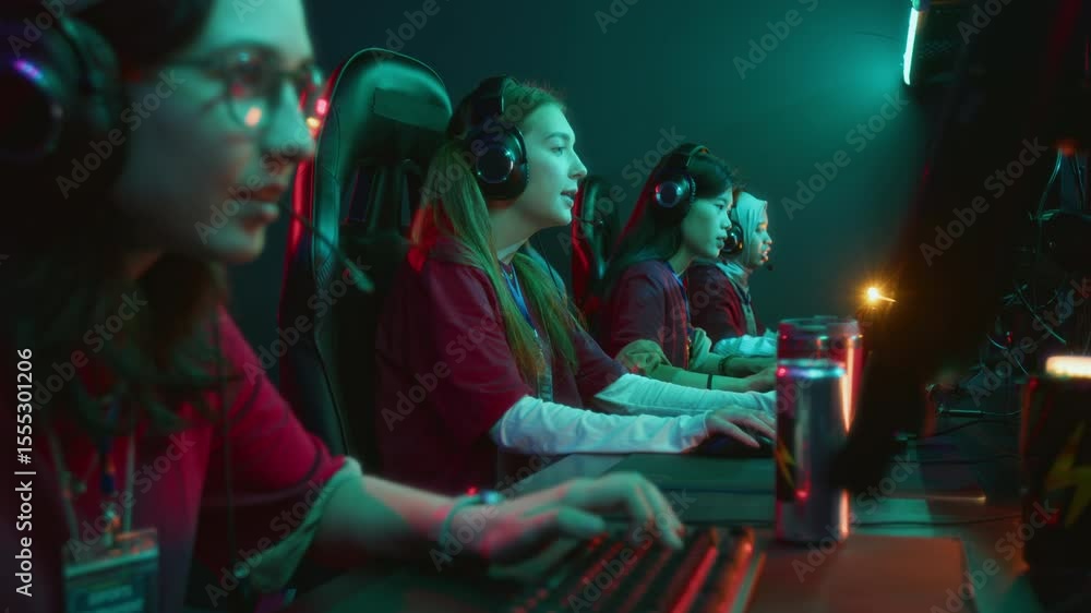 Medium side shot of cheerful young Caucasian girl with headset playing online shooter game in cyberclub with diverse female teammates, discussing and coordinating strategy Medium side shot of cheerful young Caucasian girl with headset playing online shooter game in cyberclub with diverse female teammates, discussing and coordinating strategy