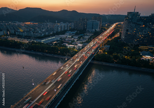 Bilde på lerret Cars traverse the illuminated blue bridge spanning the river at night with vibrant city skyline in view