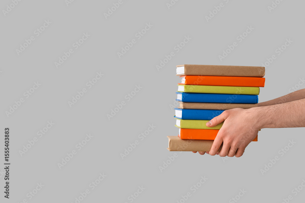 Fototapeta premium Hands holding stack of books on grey background