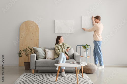 Young man hanging painting ...