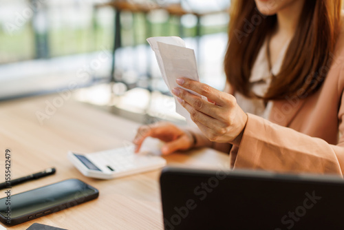 Photography asian young woman hand checking list with bill for calculate accounting expense credit card payment on due deadline, trying to find money to pay debt on table
